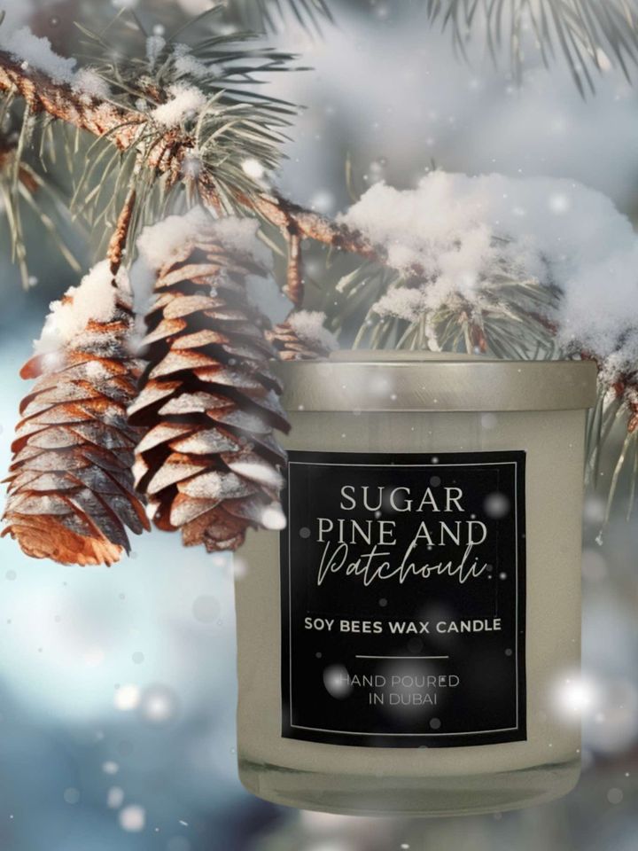 A candle with a label reading 'Sugar Pine and Patchouli' placed under a pine branch with pine cones, indicating a connection to natural scents.