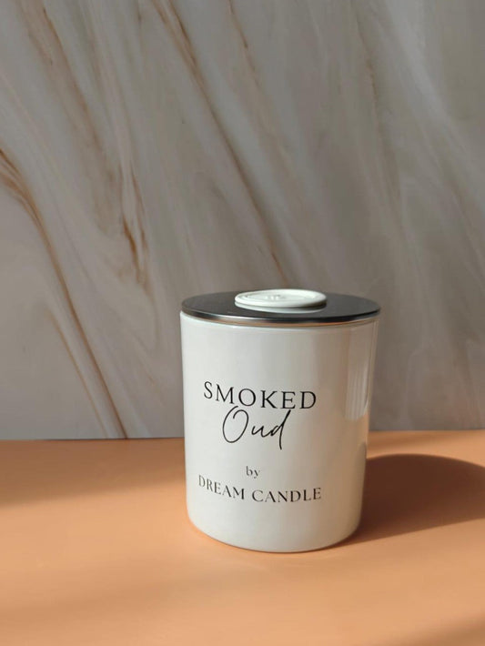 Candle labeled 'Smoked Oud by Dream Candle' on a beige surface with a marble background